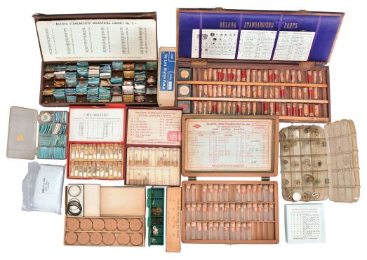 Wrist and pocket watch parts, three large boxes filled with material assortments from various manufacturers, including jewels, staffs, stems, crowns, gaskets, and more, for both Swiss and American watches, together with a box and a metal cabinet each containing hundreds of pocket watch crystals, and a wood pocket watch display case with glass door.