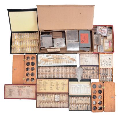 Wrist and pocket watch parts, three large boxes filled with material assortments from various manufacturers, including jewels, staffs, stems, crowns, gaskets, and more, for both Swiss and American watches, together with a box and a metal cabinet each containing hundreds of pocket watch crystals, and a wood pocket watch display case with glass door.