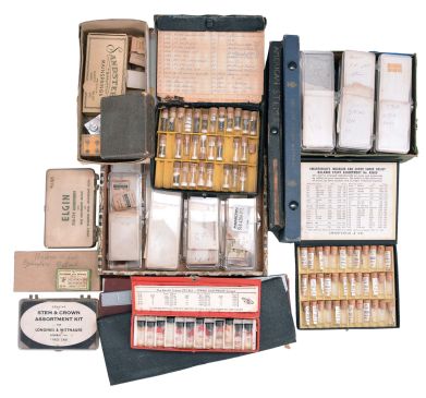 Wrist and pocket watch parts, three large boxes filled with material assortments from various manufacturers, including jewels, staffs, stems, crowns, gaskets, and more, for both Swiss and American watches, together with a box and a metal cabinet each containing hundreds of pocket watch crystals, and a wood pocket watch display case with glass door.