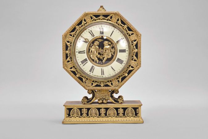 E. F. Caldwell, New York, a gilt and patinated bronze table clock, the base with leaf and dart molding, inset panels with alternating anthemion and palmette ornament, supporting a scallop shell with flanking scrolls and surmounted by the octagonal clock case, also with classical ornament, Roman numeral white enamel dial with central, gilt plaque featuring putti with garlands, gilt, engraved hands, and 8 day Chelsea timepiece movement, serial #134868