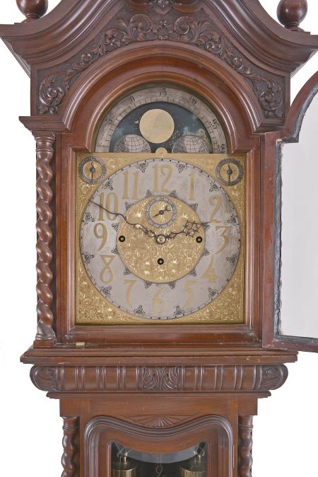 Tall clock, 8 day weight driven movement, time, strike and chime on gongs, in an elaborately carved mahogany case with broken arch top surmounted by three carved finials including center flaming urn, twist columns flanking hood and trunk doors, both of which have beveled glasses, fretwork sides on hood, over a base with carved Northwind center panel and resting on paw feet. The brass dial has silvered chapter ring, applied brass numerals, moon phase, seconds bit, and strike / silent and tune selection discs.