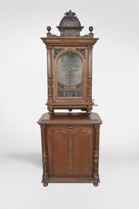 Polyphon Musicwerk, Leipzig, Germany, "Model 104" floor-standing, coin-operated disc music box, playing 19-5/8 inch discs, robust dual comb movement starting upon insertion of a U. S. quarter or Deutschmark piece, the case of mixed walnut and mahogany veneers and solids, all resting on a base cabinet with hinged, locking door. Approximately 2 dozen discs are included.