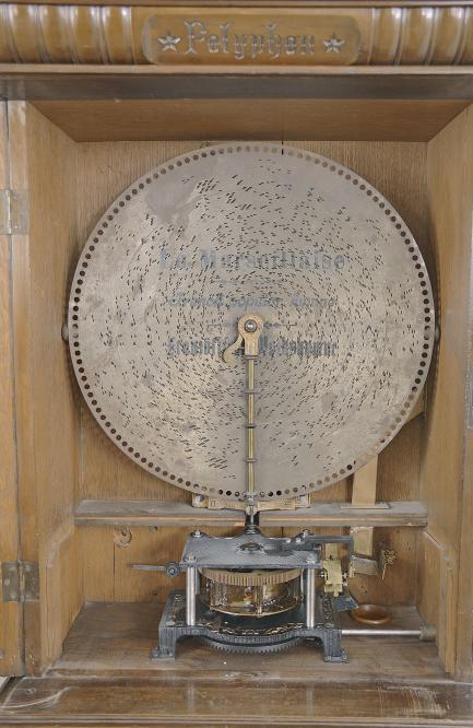 Polyphon Musicwerk, Leipzig, Germany, "Model 104" floor-standing, coin-operated disc music box, playing 19-5/8 inch discs, robust dual comb movement starting upon insertion of a U. S. quarter or Deutschmark piece, the case of mixed walnut and mahogany veneers and solids, all resting on a base cabinet with hinged, locking door. Approximately 2 dozen discs are included.