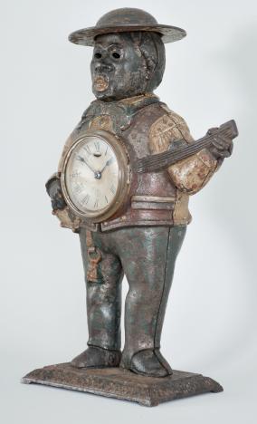 Waterbury Clock Co., "Sambo" blinking eye novelty clock, 30 hour, spring driven balance wheel movement with linkage to animate eyes in a painted cast iron case depicting a man with a banjo, roman numeral paper dial with blackened steel spade hands.