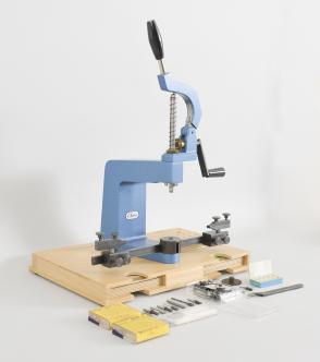 Elma Schmidbauer GmbH, Germany, KWM Universal Bushing System, clock bushing machine with lever operated quill, brass bevel gears, floating jaws, reamer / anvil / pusher set, and boxed sets of KWM brass bushings, all on wood base with dedicated spots for holding tools and supplies.