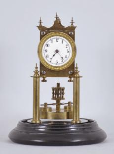 Urania / Jahresuhrenfabrik, Triberg, Germany, 400-day clock, year running, time only, spring driven movement with torsion disc pendulum on brass posts mounted to a black turned wood base, arabic numeral white enamel dial with back steel spade hands, all under a glass dome.