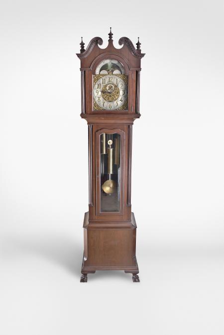 Hall Clock, 8 day, time, strike and chime on five tubular bells, three weight driven movement by Elite (German made) in a mahogany case with three finials surmounting broken arch top with dentil molding, full fluted columns flanking hood and fretwork sides over a shaped trunk door inset with beveled glass flanked by two three-quarter fluted columns over chamfered base resting on ball and claw feet. The brass dial has silvered chapter ring, engraved corner spandrels, applied brass numerals, strike / silent selector and moon phase.