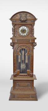 Gazo Family Clock Factory Co., National City, California, "Rancho Santa Fe" tall clock, 8 day, time, strike and chime, playing three tunes on gongs, the weight driven movement in a carved oak case with embossed brass dial, matching weights and pendulum bob, dial with roman numeral white enamel cartouches.