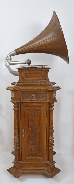 The Gramophone & Typewriter Ltd., 21 City Rd, Finsbury Square, London, England, the English subsidiary of Victor Talking Machine Co., "Type D" oak cased phonograph with original 21" diameter oak horn, 21" resting on an oak and quarter sawn oak record cabinet with single drawer over a single cabinet flanked by full turned columns flanking panels with carved musical trophies. Includes three albums of records.