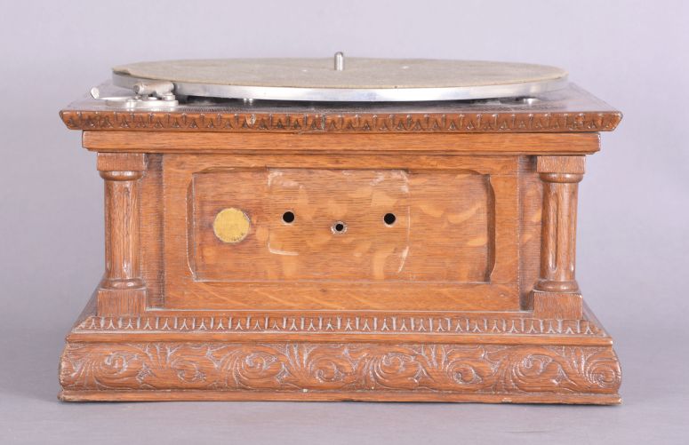 The Gramophone & Typewriter Ltd., 21 City Rd, Finsbury Square, London, England, the English subsidiary of Victor Talking Machine Co., "Type D" oak cased phonograph with original 21" diameter oak horn, 21" resting on an oak and quarter sawn oak record cabinet with single drawer over a single cabinet flanked by full turned columns flanking panels with carved musical trophies. Includes three albums of records.