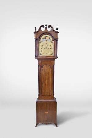 Tall clock, probably English, 8 day, time, strike weight driven movement with Westminster chime on auxiliary movement, in an inlaid mahogany case with broken arch top, three wooden finials, full fluted columns flanking hood over tombstone trunk door with string and shell inlay, flanked by fluted quarter columns resting on a base with string and shell inlay and flared French feet. The unsigned painted metal dial has moon phase, date calendar and painted rose spandrels.