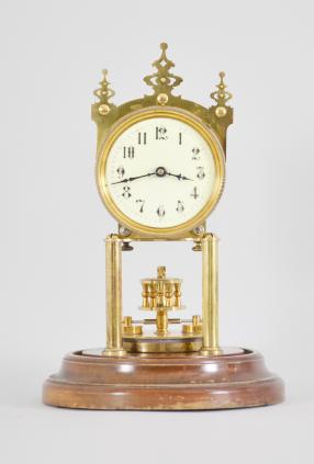 Gustav Becker, Freiburg, Germany, 400-day clock, year running, time only, spring driven brass movement with torsion pendulum and deadbeat escapement with Vulliamy pallets, brass posts holding an arabic numeral cream colored enamel dial, blued steel poker hands, all on a turned wood base under a glass dome.