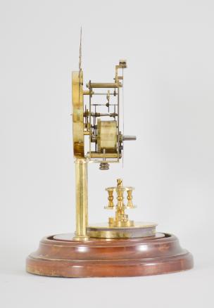 Gustav Becker, Freiburg, Germany, 400-day clock, year running, time only, spring driven brass movement with torsion pendulum and deadbeat escapement with Vulliamy pallets, brass posts holding an arabic numeral cream colored enamel dial, blued steel poker hands, all on a turned wood base under a glass dome.