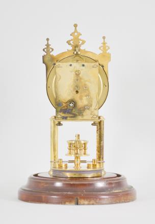 Gustav Becker, Freiburg, Germany, 400-day clock, year running, time only, spring driven brass movement with torsion pendulum and deadbeat escapement with Vulliamy pallets, brass posts holding an arabic numeral cream colored enamel dial, blued steel poker hands, all on a turned wood base under a glass dome.