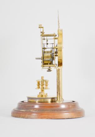 Gustav Becker, Freiburg, Germany, 400-day clock, year running, time only, spring driven brass movement with torsion pendulum and deadbeat escapement with Vulliamy pallets, brass posts holding an arabic numeral cream colored enamel dial, blued steel poker hands, all on a turned wood base under a glass dome.