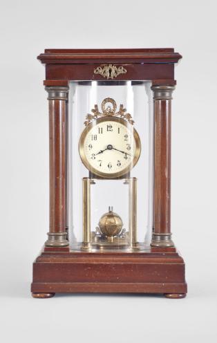 Gustav Becker, Freiburg, Germany, 400-day clock, year running, time only, spring driven movement in a four-column Empire style mahogany case with hinged top and central glass cylinder, arabic numeral white enamel dial, blued steel poker hands, and disc pendulum topped with brass sphere. 
