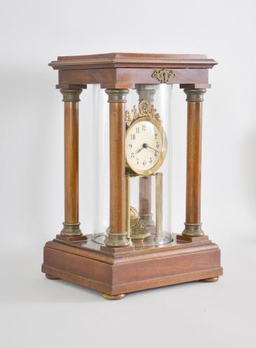 Gustav Becker, Freiburg, Germany, 400-day clock, year running, time only, spring driven movement in a four-column Empire style mahogany case with hinged top and central glass cylinder, arabic numeral white enamel dial, blued steel poker hands, and disc pendulum topped with brass sphere. 
