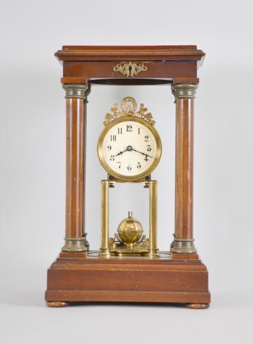 Gustav Becker, Freiburg, Germany, 400-day clock, year running, time only, spring driven movement in a four-column Empire style mahogany case with hinged top and central glass cylinder, arabic numeral white enamel dial, blued steel poker hands, and disc pendulum topped with brass sphere. 
