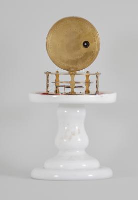 Terryville Manufacturing Company, Terryville, Conn., candle stand clock, 30 hour, time only, spring driven brass movement with four-arm balance wheel movement, 2.75 inch paper on zinc dial signed "Terryville Mfg. Co. / Terryville / Conn.", black steel hands, all on a white milk glass pedestal under small glass dome.