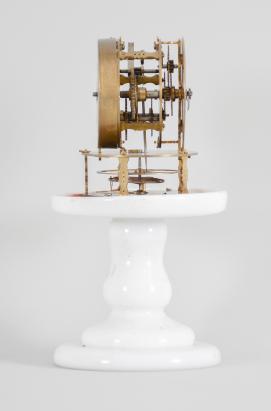 Terryville Manufacturing Company, Terryville, Conn., candle stand clock, 30 hour, time only, spring driven brass movement with four-arm balance wheel movement, 2.75 inch paper on zinc dial signed "Terryville Mfg. Co. / Terryville / Conn.", black steel hands, all on a white milk glass pedestal under small glass dome.