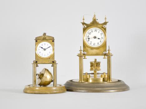 Clocks- 2 (Two) miniature 400-day (1) Phillip Hauck, Munich, Germany, "Semester Uhr" or half-year clock, 200-day, time only, spring driven movement with torsion disc pendulum on a brass base, arabic numeral white enamel dial, under small glass dome, c1906; (2) Kienzle GmbH, Schwenningen, Germany, miniature torsion pendulum clock, 30 day, time only, spring driven movement pin-pallet escapement and semi-spherical torsion pendulum on a polished stone base and under a glass dome, c1910.