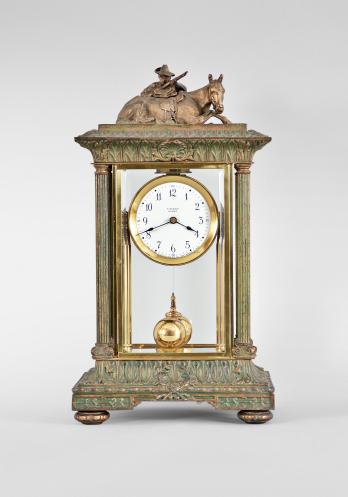 Tiffany Electric Mfg. Co., New York, NY, "Tiffany Electric" large mantel clock, battery-powered movement with torsion pendulum in a glazed crystal regulator style case with leaf-and-dart molded base and top, four fluted columns at the corners, surmounted by the cast figure of a cowboy crouched behind his horse with his rifle, arabic numeral white enamel dial, black steel spade hands, and two-ball polished brass pendulum.