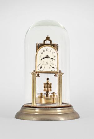 Kienzle GmbH, Schwenningen, Germany, 400-day clock for the French market, year running, time and calendar, spring driven brass movement with torsion pendulum, arched enamel dial with arabic numerals and subsidiary dials for day of the month and day of the week, black steel spade hands, all under a glass dome.