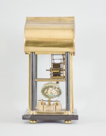 Jahresuhrenfabrik, Triberg, Germany, 400-day clock, year running, time only, spring driven movement with torsion pendulum disc on a polished stone base with four columns supporting a curved brass roof, the central portion containing the clock is glazed on four sides, arabic numeral white enamel dial, black steel spade hands.