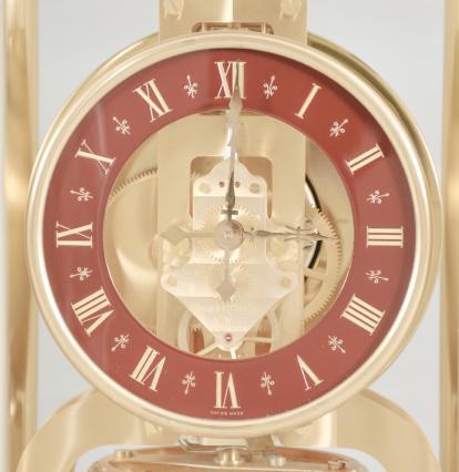 Jaeger-LeCoultre, Switzerland, Atmos perpetual clock, 528 caliber, jeweled movement with torsion pendulum in a polished brass case with curved acrylic panels, round maroon enamel dial with incised roman numerals, and polished brass hands.