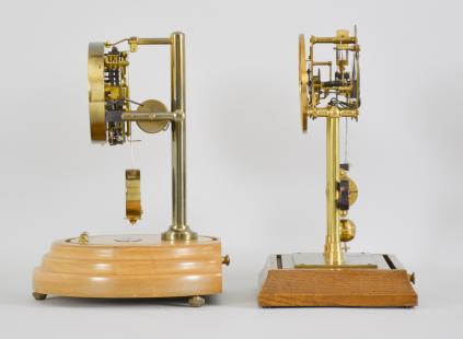 Clocks- 2 (Two) Electromechanical shelf clocks (1) England, mantel clock, battery powered movement electromagnet pendulum encircling a segment of permanent magnet, skeletonized brass movement on two posts mounted to a molded wood base, arabic numeral silvered dial, black steel hands, all under an clear acrylic box with arched top, c1935; (2) Barr Mfg. Corp., Weedsport, NY, mantel clock, electric battery movement in a brass frame, silvered dial with subsidiary seconds, black steel hands, all under a glass dome resting on a turned wood base, c1938.