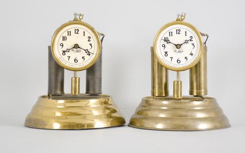 Clocks- 2 (Two) Mountain State Electrical Co., Wheeling, W. Virginia, "No-Key" clocks, weight driven brass movements with battery powered automatic winding, brass bases, arabic numeral white celluloid dials with blackened brass hands under glass domes.