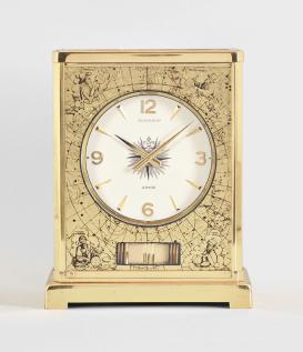 Jaeger-LeCoultre, Switzerland, "Atmos" perpetual clock, caliber 526-5, jeweled movement with torsion pendulum, round white painted dial with four applied gilt arabic numerals and arrow markers, gilt hands, all contained in a glazed rectangular case decorated on the inside with gilt maps showing antiquated representations of the constellations.