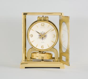 Jaeger-LeCoultre, Switzerland, "Atmos" perpetual clock, caliber 526-5, jeweled movement with torsion pendulum, round white painted dial with four applied gilt arabic numerals and arrow markers, gilt hands, all contained in a glazed rectangular case decorated on the inside with gilt maps showing antiquated representations of the constellations.