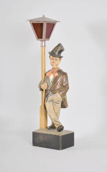 Karl Griesbaum, Triberg, Germany, carved "Hobo" or "Drunkard" whistling figure, spring driven brass movement driving a bellows, cam-controlled slide whistle, and head turn motion enclosed in a hand carved wood figure depicting an inebriated man in a top hat who leans on a lamp post, the top of which contains a battery powered bulb behind red glass.