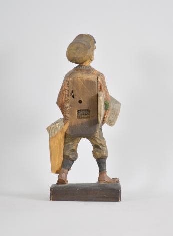 Karl Griesbaum, Triberg, Germany, "Newsboy" whistling figure, spring driven brass movement driving a bellows, cam-controlled slide whistle, and head motion, enclosed in a hand carved wood figure depicting a boy in a flat cap and nickers with a newspaper under one arm and a bag full of papers hanging at his side.