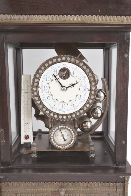 Reproduction Ferris wheel gravity timepiece, 8 day, time only, weight driven balance wheel movement in a glazed wood case with applied brass ornaments, polychrome enamel dial, a small barometer dial below, and alcohol thermometer adjacent, all surmounted by a patinated brass lion.