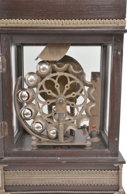 Reproduction Ferris wheel gravity timepiece, 8 day, time only, weight driven balance wheel movement in a glazed wood case with applied brass ornaments, polychrome enamel dial, a small barometer dial below, and alcohol thermometer adjacent, all surmounted by a patinated brass lion.