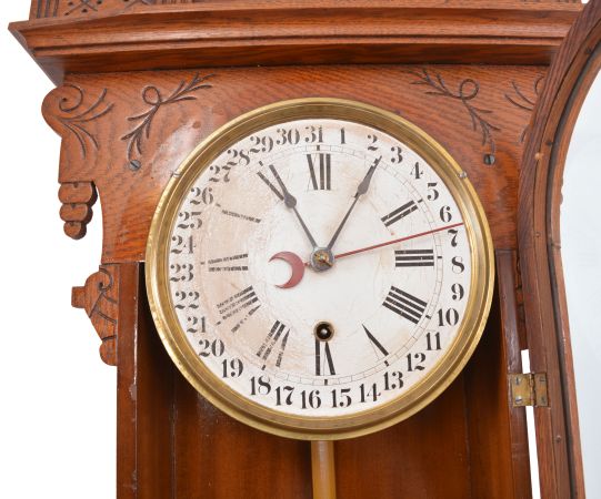 Ansonia Clock Co., New York, for Metropolitan Manufacturing Co., "Eclipse" hanging gingerbread clock, 8 day, time and simple calendar, spring driven movement in an oak case.