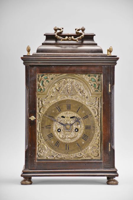 Austria, a late 18th century, repeating bracket clock with mock pendulum, ebonized hardwood case on compressed, silvered ball feet, plain rectangular door allowing a veiw of the decorative dial, molded top with brass finials and caddy top with brass handle, case sides with tombstone arch windows, and back also with rectangular, glazed door, silvered repousse dial with C scrolls, flowers, and bowknot with laurel festoon, the upper corners pierced, and with green paper backing, brass roman numeral chapter ring with arabic five minute markers, blued steel beetle and poker hands, 30- 60 hour brass movement with crown wheel escapement, rack striking, and repeating the last hour on demand