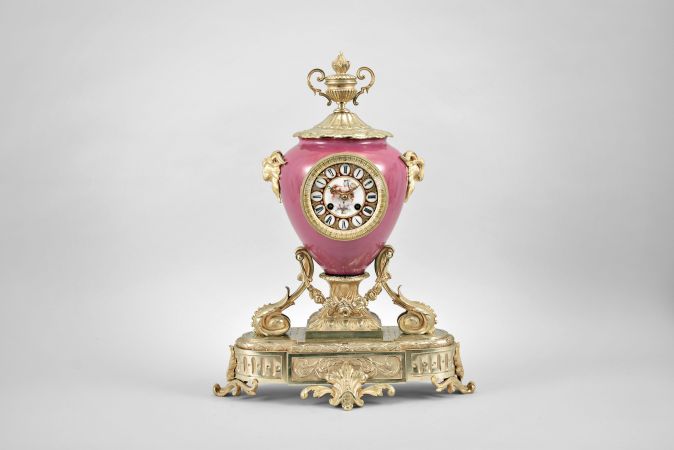 France, ceramic and ormolu mantel clock, 8 day, time and strike, spring driven pendule de Paris movement in a vibrant porcelain vase-form case mounted on a gilt metal base with floral swag, flanked by horned rams, and topped with an urn finial, polychrome painted dial with putto, gilt hands.