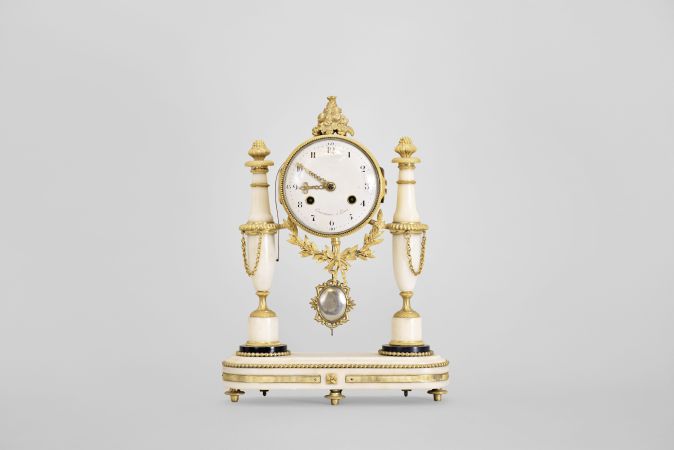 Courvoisier, a Paris, a late 18th century marble and gilt bronze mantel clock, the oblong base on toupie feet with inset, reeded mounts and central foliate ornament, and finished with a gilt bead molding, the gilt clock case with laurel and bowknot drop, and surmounted by a pyramid of fruit, the case supported bu two slender vasiform columns, with foliate and basket weave mounts, and gadrooned rings, arabic numeral white enamel dial, signed "Courvoisier a Paris", well executed pierced and engraved gilt hands, 8 day two train movement with crown wheel escapement, the Swiss style strike work mounted to the back plate, and with silk thread suspension, repeating the last hour on demand