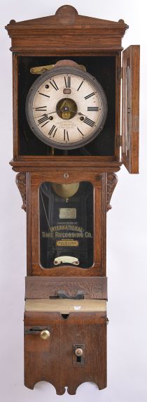 International Time Recording Co., Endicott, NY sold by James & Co., Rochester N.Y., wall hanging punch clock, 8 day, time and day of the week, spring driven movement in an oak case with punch mechanism and painted metal dial with exposed center and day of the week aperture