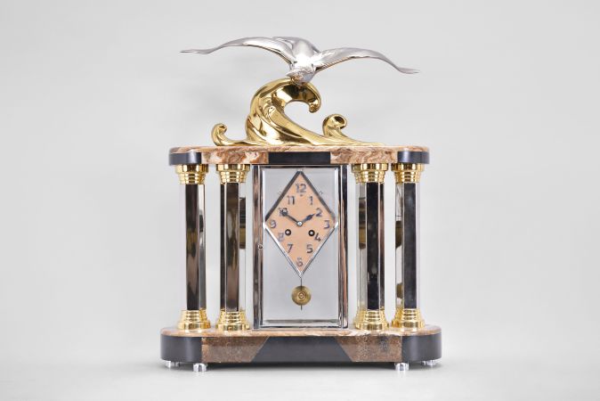 Michel Decoux, a marble and polished metal mantel clock with gull ornament, the oblong base and top with brown, variegated marble veneers over contrasting black slate base and panels, joined portico style by six hexagonal, polished chrome columns with polished, gilt capitals and bases, and flanking a polished chrome crystal regulator case, surmounted by a polished, gilt wave form casting and polished chrome gull, signed "Decoux", diamond shaped Arabic numeral metal dial with blued steel hands, and 8 day Pendule de Paris movement, striking on a bell