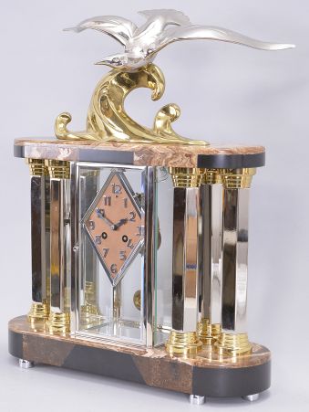 Michel Decoux, a marble and polished metal mantel clock with gull ornament, the oblong base and top with brown, variegated marble veneers over contrasting black slate base and panels, joined portico style by six hexagonal, polished chrome columns with polished, gilt capitals and bases, and flanking a polished chrome crystal regulator case, surmounted by a polished, gilt wave form casting and polished chrome gull, signed "Decoux", diamond shaped Arabic numeral metal dial with blued steel hands, and 8 day Pendule de Paris movement, striking on a bell