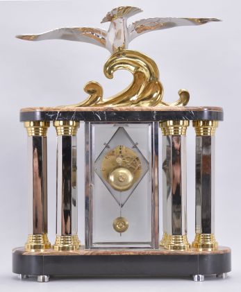 Michel Decoux, a marble and polished metal mantel clock with gull ornament, the oblong base and top with brown, variegated marble veneers over contrasting black slate base and panels, joined portico style by six hexagonal, polished chrome columns with polished, gilt capitals and bases, and flanking a polished chrome crystal regulator case, surmounted by a polished, gilt wave form casting and polished chrome gull, signed "Decoux", diamond shaped Arabic numeral metal dial with blued steel hands, and 8 day Pendule de Paris movement, striking on a bell