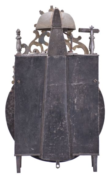 France, Comtoise lantern clock, 8 day, time and strike with alarm, weight driven movement with verge escapement, thread suspension with rear-hanging pendulum in an iron post and plate frame, early faïence dial with raised portions under each Roman numeral, outer ring with Arabic numerals every five minutes, two steel hands, brass alarm ring with Arabic numerals, topped by a cast brass fronton with image of the sun / Apollo flanked by two turned iron finials, all standing on tapered iron feet.