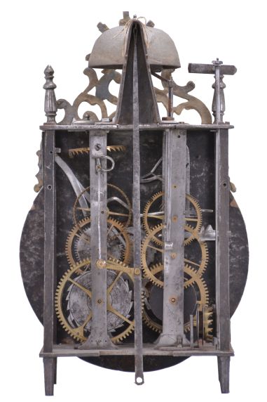 France, Comtoise lantern clock, 8 day, time and strike with alarm, weight driven movement with verge escapement, thread suspension with rear-hanging pendulum in an iron post and plate frame, early faïence dial with raised portions under each Roman numeral, outer ring with Arabic numerals every five minutes, two steel hands, brass alarm ring with Arabic numerals, topped by a cast brass fronton with image of the sun / Apollo flanked by two turned iron finials, all standing on tapered iron feet.