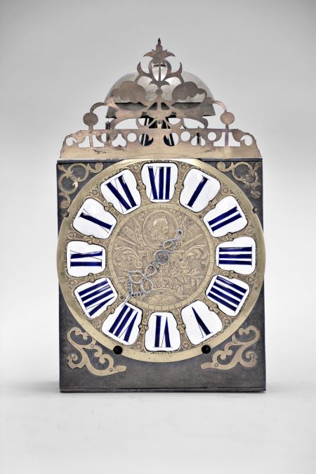 France, Comtoise clock, 8 day, time and strike, weight driven movement, verge escapement, thread suspension with rear-hanging pendulum in an iron post and plate frame, cast brass dial with royal symbols including a crown resting on the earth and profile of a young Louis XV or his son The Dauphin, white enamel cartouches with blue Roman numerals, single iron hand, four flat brass spandrels, topped by pierced flat brass fronton, mid 18th Century.