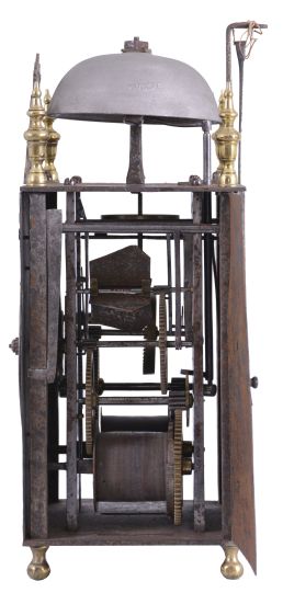 France, Comtoise lantern clock, 8 day, time and strike, weight driven movement with verge escapement, thread suspension with rear-hanging pendulum in a iron post and plate frame, pewter chapter ring with engraved Roman numerals, single brass hand, applied brass fleur de lis spandrels and pivoted winding arbor shutters, all resting on four turned brass feet, and topped by flat pierced brass fronton flanked by four turned brass finials.