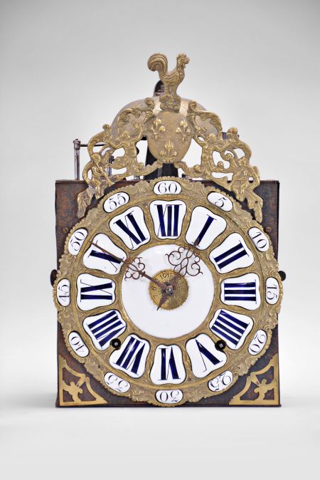 France, bronze-front Comtoise clock, 8 day, time and strike with alarm, weight driven movement, verge escapement with thread suspension and rear-hanging pendulum in an iron post and plate frame, cast brass dial with inset white enamel cartouches with blue Roman numerals for the hours and black Arabic numerals for the minutes, brass alarm ring with Arabic numerals, two pierced steel hands, applied brass spandrels below the dial, and topped with a cast fronton featuring a forward facing Gallic rooster over a medallion with three fleur de lis.